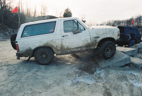 1995 Ford Bronco - White 1995 Ford Bronco navigating an obstacle course with a dark SUV in the background.