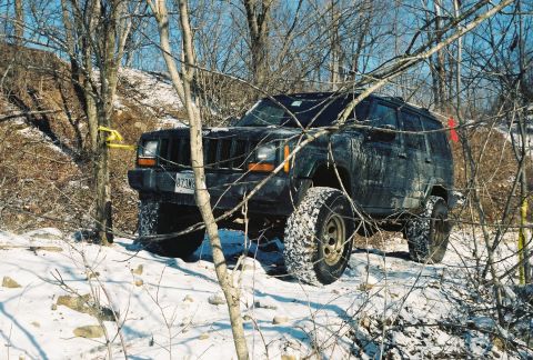 1995 Ford Bronco - A black Jeep Cherokee XJ navigates a snowy, wooded trail with bare trees.