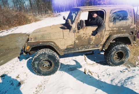 1995 Ford Bronco - A driver navigates a muddy Jeep Wrangler through a snowy and muddy trail.