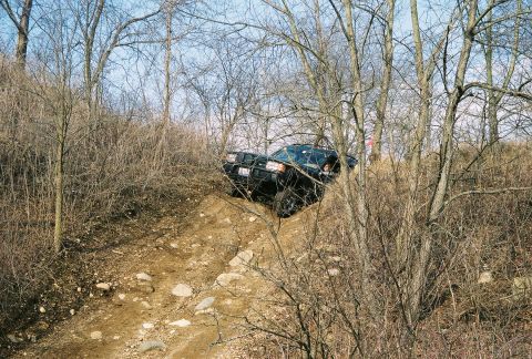 1995 Ford Bronco - Black 1995 Ford Bronco navigates a challenging off-road course on a sunny day.