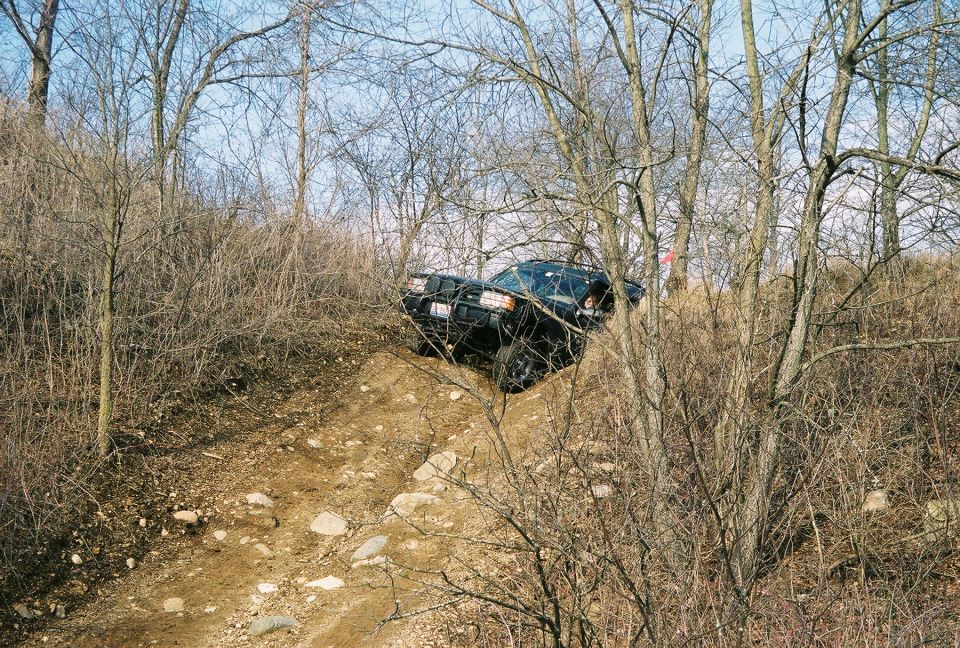 1995 Ford Bronco climbing a steep, rocky dirt trail through bare trees