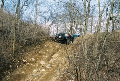 1995 Ford Bronco - Two vehicles navigate a challenging off-road trail through a wooded area.