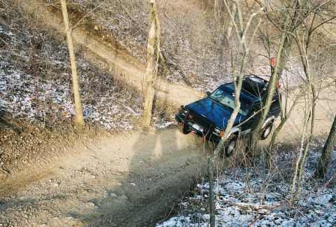 1995 Ford Bronco - A blue SUV navigates a wooded trail with snow on the ground.