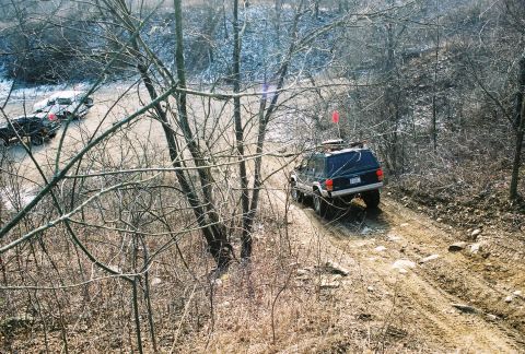 1995 Ford Bronco - A Jeep Cherokee XJ navigates a challenging off-road trail, with another vehicle visible in the background.