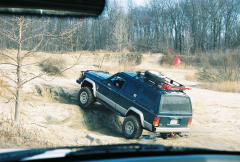 1995 Ford Bronco - Off-road vehicle navigating a challenging rocky terrain with trees in the background.