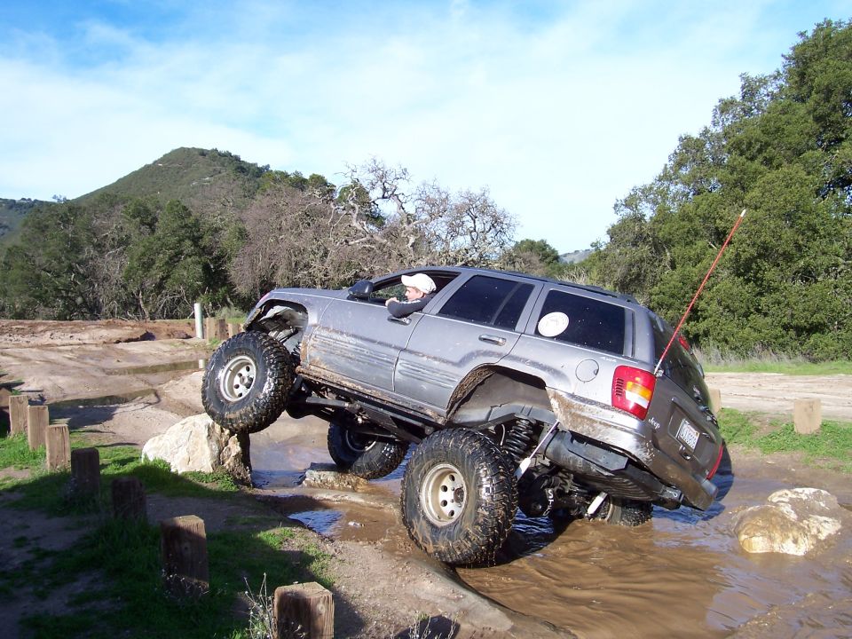 Silver Jeep Grand Cherokee with lifted suspension and large tires navigating an off-road obstacle course