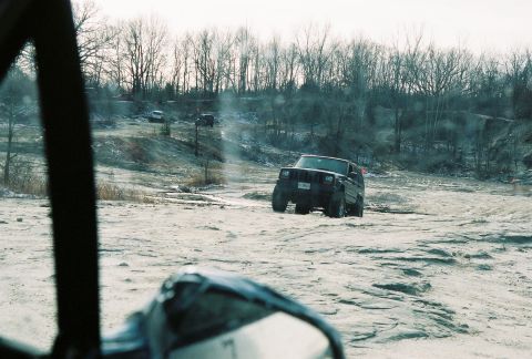 1995 Ford Bronco - A dark SUV navigates a rough, snowy terrain with other vehicles visible in the background.