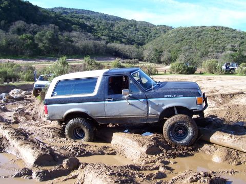 1998 Ford Ranger - Ford Bronco tackling a challenging muddy terrain, with another vehicle in the distance.