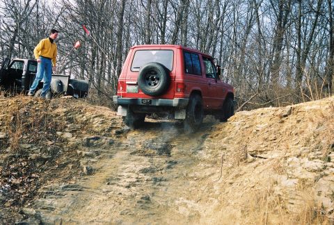 1995 Ford Bronco - A red SUV navigates a steep, rocky incline during an off-road excursion.