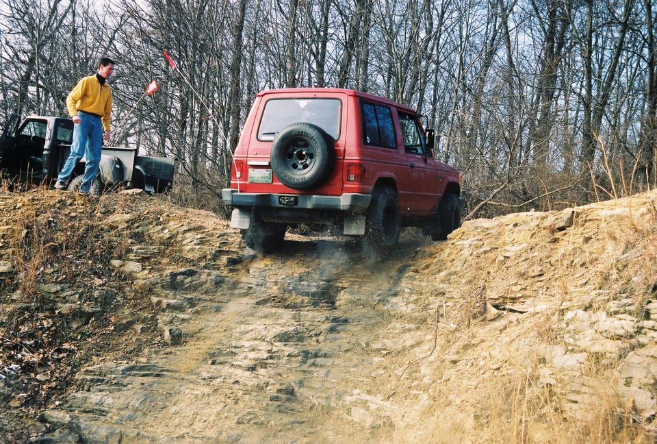 Red SUV climbing dirt hill, spare tire on rear door