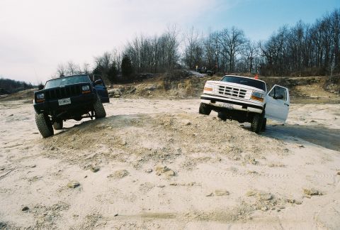 1995 Ford Bronco - Two trucks navigate a challenging off-road course on a sunny day.