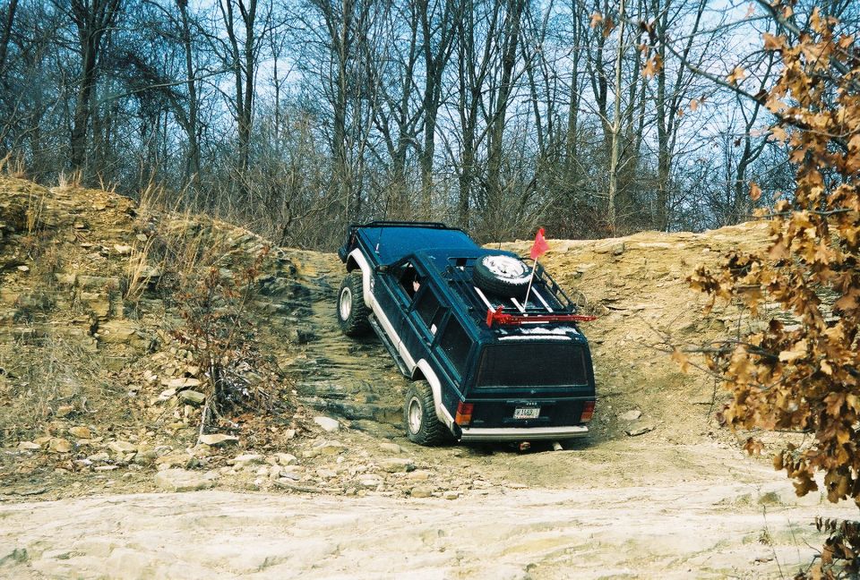 Dark blue SUV with spare tire on roof rack climbing a dirt hill