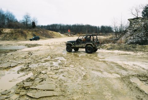 1995 Ford Bronco - Off-road Jeeps navigate a challenging muddy landscape with a quarry-like environment.