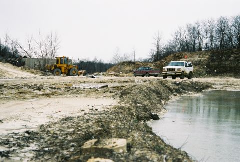 1995 Ford Bronco - A white SUV and a red pickup truck are parked at a muddy construction site with a yellow loader in the background.