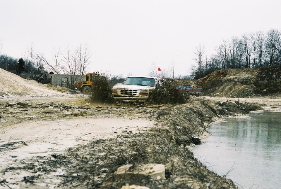 1995 Ford Bronco driving through a muddy area with a yellow loader in the background