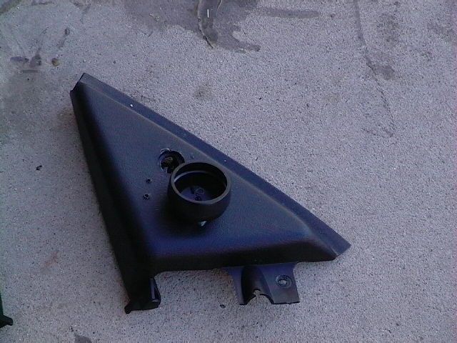 Black plastic trim piece, possibly for a car's side mirror assembly, lying on concrete