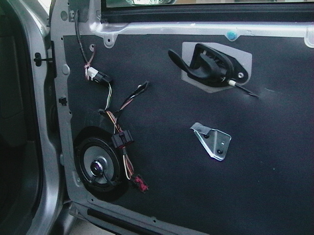 Car door panel with speaker removed, showing wiring and door handle mechanism