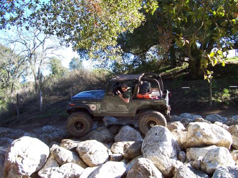 1998 Ford Ranger - A Jeep CJ-7 tackles a challenging rocky terrain under a canopy of trees.