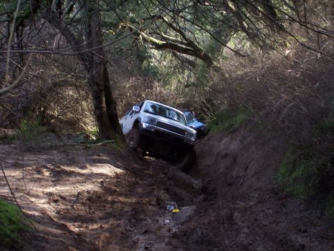 1998 Ford Ranger - A white pickup truck struggles on a muddy, off-road trail, with a second vehicle partially visible behind it.