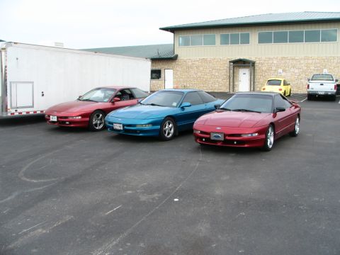 1994 Ford Probe - Three Ford Probes are parked in front of a building. A yellow Volkswagen Beetle and a white pickup truck are also visible.