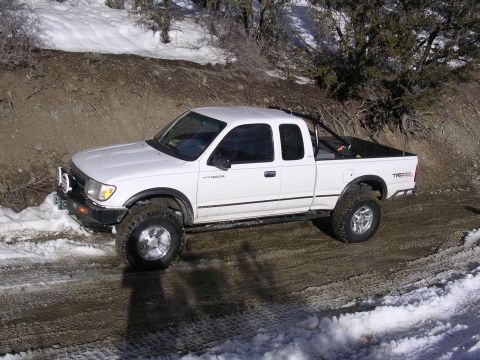 1999 Toyota Tacoma - A white 1999 Toyota Tacoma pickup truck navigates a snowy and muddy road in a wooded area.