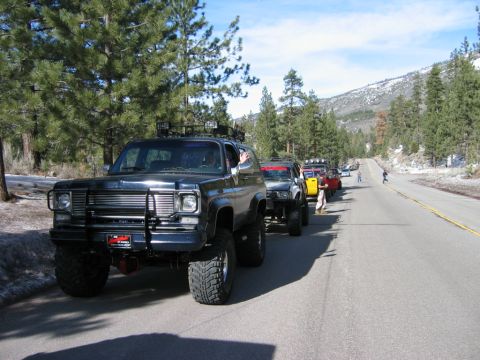 1999 Toyota Tacoma - A line of off-road vehicles, including a dark blue SUV with a brush guard and roof rack, travel down a mountain road.