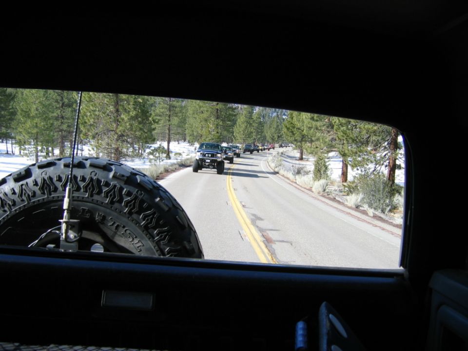 View from inside a vehicle looking out at a line of SUVs driving on a road with snow on the sides