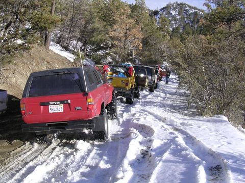 1999 Toyota Tacoma - A line of off-road vehicles, including a red Toyota SUV, navigate a snow-covered mountain trail.