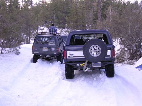 1999 Toyota Tacoma - A dark SUV, identified as a Toyota, navigates a snowy terrain with a person seated on its roof rack.