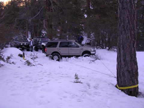 1999 Toyota Tacoma - Multiple SUVs are stuck in the snow, with one vehicle being winched to a tree for extraction.