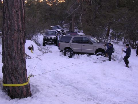 1999 Toyota Tacoma - People work to free vehicles stuck in a snowy, wooded area, using a winch and shovels.