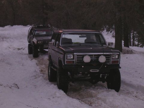 1999 Toyota Tacoma - Two off-road vehicles navigate a snow-covered path through a wooded area.