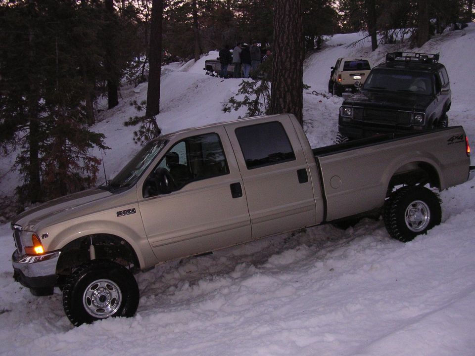 Tan pickup truck with lifted suspension in snow. Visible text on fender reads "F-250"