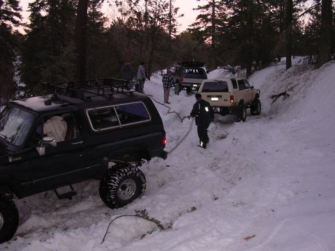 1999 Toyota Tacoma - Multiple off-road vehicles are stuck in the snow on a steep, wooded trail.