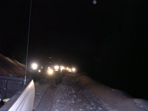 1999 Toyota Tacoma - A convoy of trucks navigates a dark, off-road path at night, their headlights cutting through the darkness.