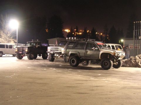 1999 Toyota Tacoma - Multiple modified trucks and SUVs are parked together outdoors at night under bright lights.