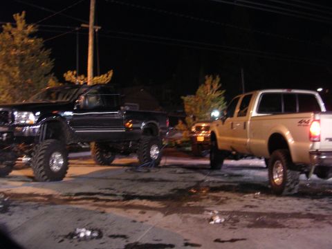 1999 Toyota Tacoma - Two heavily modified pickup trucks are parked outside at night, illuminated by streetlights.