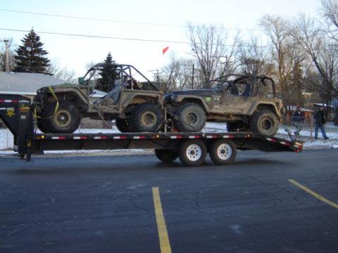 1992 Ford Bronco - Two muddy off-road vehicles are transported on a flatbed trailer.