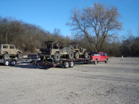 1992 Ford Bronco - A red pickup truck tows a trailer loaded with two off-road vehicles, with another off-road vehicle on a second trailer.