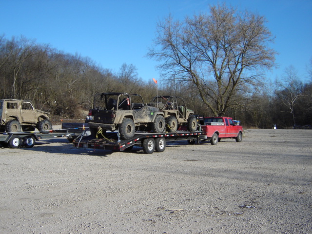 Red pickup truck towing a trailer with two off-road vehicles, another off-road vehicle on a separate trailer behind it
