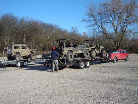 1992 Ford Bronco - Multiple off-road vehicles are transported on a trailer, with a person standing near one of them.