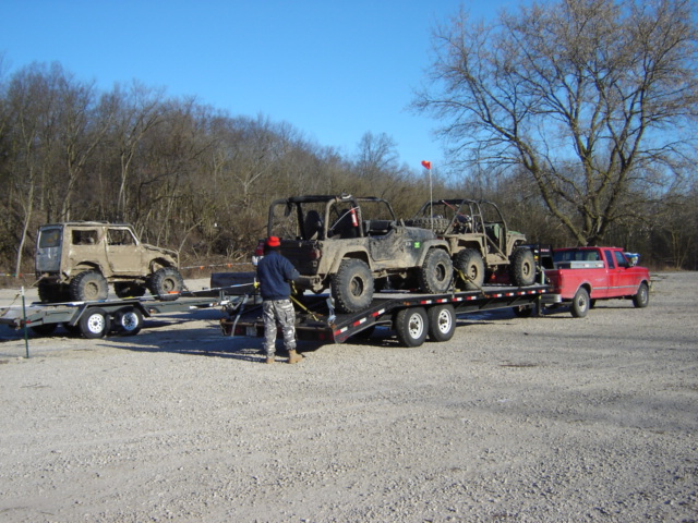 Off-road vehicles loaded onto a dual-axle trailer towed by a red pickup truck