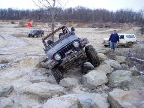 1992 Ford Bronco - A Jeep Wrangler tackles a challenging rocky obstacle course with other vehicles in the background.