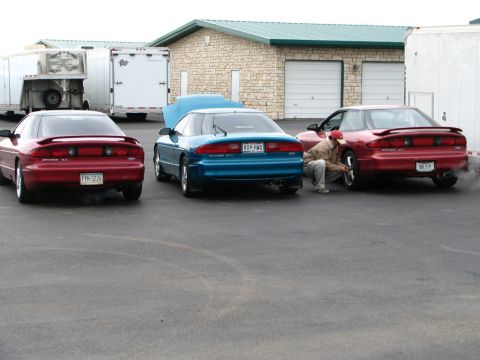 1994 Ford Probe - Three Ford Probes are parked in a lot near a building, with one person attending to a tire on the rightmost car.