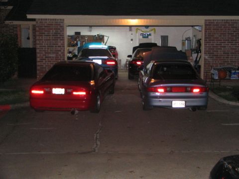 1994 Ford Probe - Multiple vehicles are parked in front of an open garage door at night.