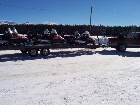 1994 Ford Bronco - A pickup truck tows a trailer loaded with multiple snowmobiles through a snowy area.