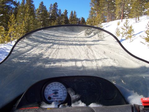 1994 Ford Bronco - View from a snowmobile dashboard as it travels down a groomed, snowy trail in a forest.