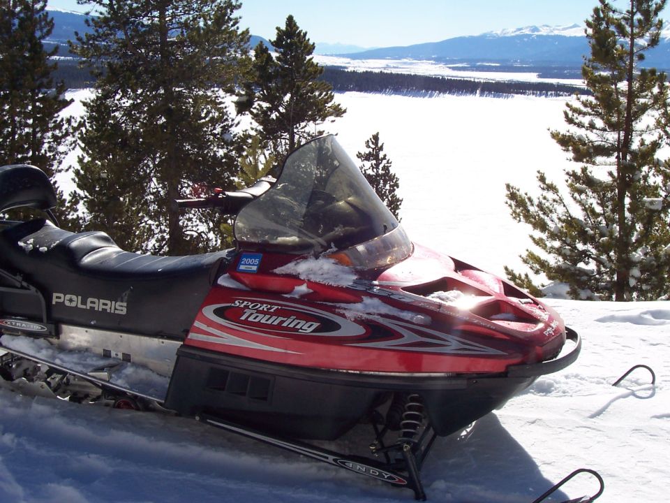 Red Polaris Sport Touring snowmobile with a 2008 badge, parked in snow with trees and a frozen lake in the background