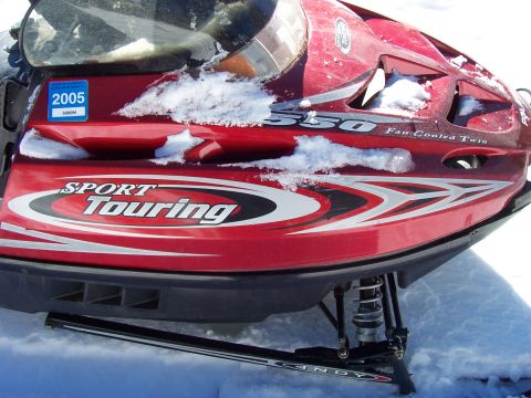 1994 Ford Bronco - A red snowmobile, identified as a 'Sport Touring' model, is partially covered in snow, with a 2005 sticker visible on its hood.