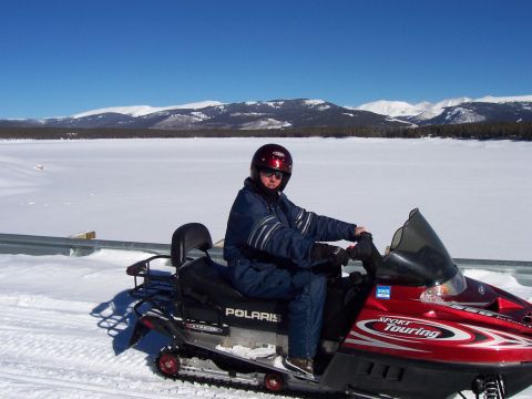 1994 Ford Bronco - A person rides a red Polaris snowmobile across a snowy landscape with mountains in the background.